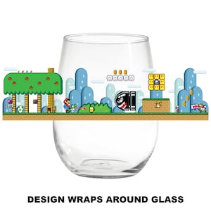 May include: A clear glass wine glass with a design of a video game level wrapped around it. The design features a green tree, blue clouds, a red character, and a yellow and black enemy.