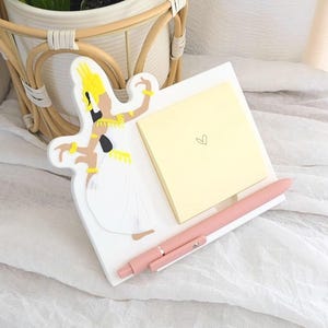 May include: A white decorative tray featuring a stylized dancer figure, a yellow sticky note with a heart, and a pink pen. The dancer has yellow and black accents. The pen is approximately 5.5 inches long.
