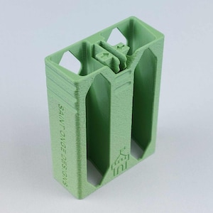 May include: A light green, rectangular 3D-printed object with a textured surface. The object has two open compartments and a central locking mechanism. The text "SAINT ONGE DESIGNS" is printed vertically on the side, and a logo is visible.