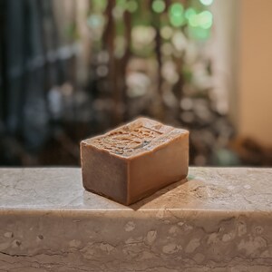 May include: A rectangular bar of brown soap with a textured surface. The soap is sitting on a light gray marble surface.