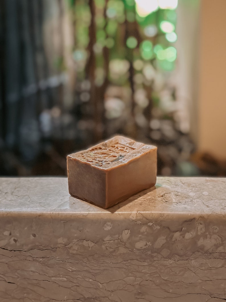 May include: A rectangular bar of brown soap with a textured surface. The soap is sitting on a light gray marble surface.