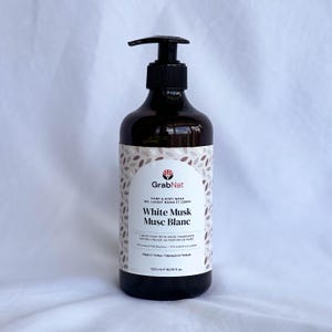 Könnte beinhalten: Eine dunkelbraune Flüssigseifenflasche mit einem schwarzen Pumpspender. Das Etikett trägt die Aufschrift "GrabNat Hand & Body Wash White Musk Musc Blanc" mit einem Blättermuster. Die Flasche enthält 500 ml Flüssigseife.