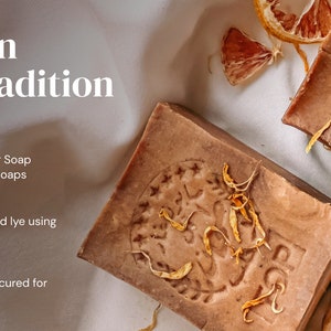 May include: Two bars of brown soap with a textured surface and a label that says "TOP". The soap is surrounded by dried orange peels and petals.