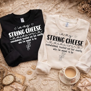Könnte beinhalten: Zwei langärmlige Sweatshirts, eines in Schwarz und eines in Creme, mit dem Text "in my STRING CHEESE mama era" und einer Grafik von Käsefäden. Der Text lautet auch "overwhelmed, touched out but exactly who I'm meant to be."