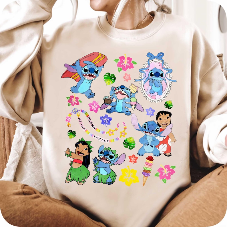 May include: Beige sweatshirt featuring a colorful graphic of the character Stitch from Lilo & Stitch. The design includes Stitch with a surfboard, ice cream, and other tropical elements. The phrase "OHANA MEANS FAMILY" is also included.