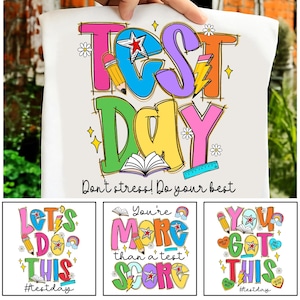 May include: A white t-shirt featuring the words "TEST DAY" in vibrant, bubble-style lettering. The design incorporates a star, pencil, lightning bolt, open book, and ruler. The phrase "Don't stress! Do your best" is below.
