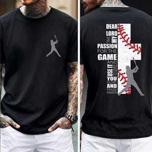 Könnte beinhalten: Schwarzes T-Shirt mit Baseball-Motiv. Auf der Vorderseite befindet sich eine graue Silhouette eines Schlagmanns und auf der Rückseite ein Baseball-Design in Kreuzform mit Text. Der Text lautet: "Dear Lord, Take My Passion For The Game And Use It To Give You Glory And Praise Amen."