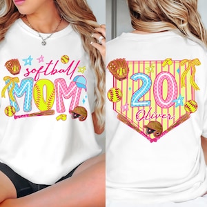 Puede incluir: Camiseta blanca con un diseño de softbol colorido. La parte delantera presenta las palabras "softball MOM" con gráficos temáticos de béisbol. La parte trasera muestra "20 Oliver" dentro de un emblema en forma de béisbol, también con elementos de softbol.