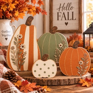 May include: A set of four decorative wooden pumpkins in various shapes and sizes. The pumpkins feature orange and cream stripes, solid sage green, and cream with green polka dots, all adorned with raised floral sprigs and dark brown stems.