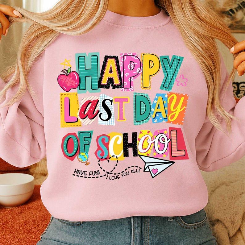 K&ouml;nnte beinhalten: Ein hellrosa Sweatshirt mit der Aufschrift "HAPPY LAST DAY OF SCHOOL" in bunten Blockbuchstaben. Das Design umfasst einen Apfel, einen Globus, ein Papierflugzeug und die S&auml;tze "HAVE FUN!" und "I LOVE YOU ALL!"