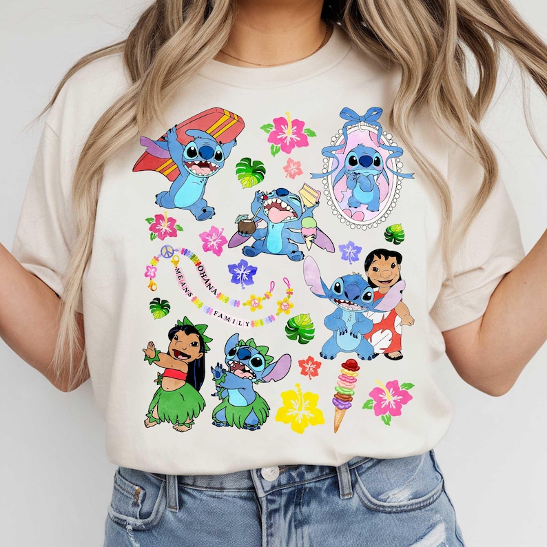 May include: A beige t-shirt featuring multiple cartoon images of a blue alien character, surrounded by flowers and the text "OHANA MEANS FAMILY". The design includes the alien with a surfboard, ice cream, and in a picture frame.