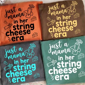 Könnte beinhalten: Vier T-Shirts in Orange, Braun, Grau und Grün, jeweils mit dem Satz "just a mama in her string cheese era" in einer verspielten Schriftart. Das Design umfasst Käse- und Käse-Grafiken.