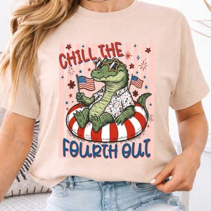 May include: A beige t-shirt featuring a cartoon alligator wearing sunglasses and a Hawaiian shirt, floating on a red and white striped inner tube. The text "Chill the Fourth Out" is printed above and below the alligator.