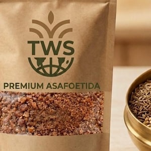 May include: A brown paper bag of premium asafoetida spice with a clear window showing the contents. The bag has the text "THREEWORLDSTORE" and "TWS" logo. The net weight is 100g. A golden bowl with spices is on the right.