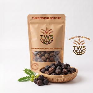 Könnte beinhalten: Ein brauner Standbeutel mit der Aufschrift THREEWORLDSTORE enthält getrocknete Amla-Stachelbeeren, sichtbar durch ein Sichtfenster. Vor dem Beutel steht ein geflochtener Bambuskorb mit dunklen, runzligen getrockneten Amla-Früchten und einem grünen Zweig.