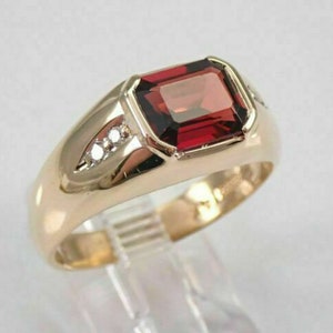 Peut inclure: Une bague en or avec une grande pierre précieuse rectangulaire rouge et des pierres précieuses plus petites et claires sur la bande.