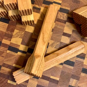 May include: Two wooden kitchen tools with a textured surface. The tools are made of light brown wood and have a rectangular shape. The tools are lying on a wooden cutting board.