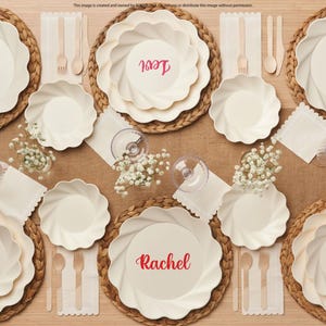 Peut inclure: Un service de table composé d'assiettes crème à bords festonnés, certaines personnalisées avec le texte rouge Levi ou Rachel, accompagné de fourchettes et cuillères en bois, de serviettes blanches et de petits bols en verre avec des fleurs.