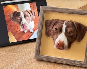 Puede incluir: Un retrato de perro afieltrado enmarcado. El perro tiene pelaje marrón y blanco, con una raya blanca en la cara. El retrato está sobre un fondo amarillo dentro de un marco de madera gris. Una imagen digital del perro es visible en una tableta.