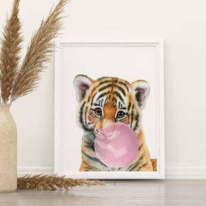 May include: A framed watercolor print features a baby tiger with orange and black stripes blowing a large pink bubble gum bubble. The artwork is set against a white background, framed in a white border.