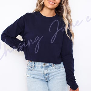 May include: A navy blue long-sleeved top with a crew neck. The top is worn with light blue denim jeans. The text "Chasing June co" is written in a cursive font across the top.