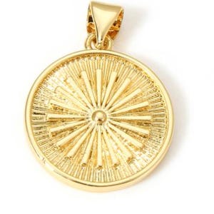 May include: A gold-colored pendant with a sunburst design. The pendant is round with a textured surface and a small loop at the top for a chain. The sunburst pattern radiates from a central point.