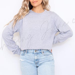 May include: A pale grey long-sleeved sweatshirt and light blue denim jeans. The sweatshirt has a crew neck and a relaxed fit. The jeans are a light wash with a classic five-pocket design. The words "Chasing June co" are written in cursive on the image.