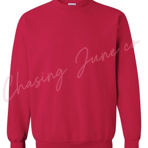 May include: A solid red crew neck sweatshirt. The long-sleeved top has a ribbed collar, cuffs, and hem. The text "Chasing June co" is written in a cursive font across the front of the sweatshirt.