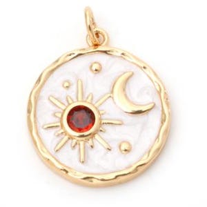 May include: Gold-tone pendant with a white enamel background. The pendant features a sun with a red center stone, a crescent moon, and small star accents. The pendant has a textured edge and a loop for a chain.