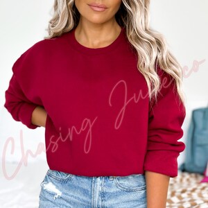 May include: A solid burgundy crewneck sweatshirt. The long-sleeved top is a deep red color. The text "Chasing June Co" is written in a cursive font on the left side of the sweatshirt.