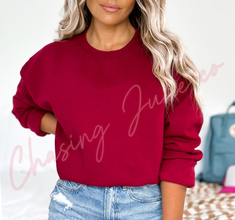 May include: A solid burgundy crewneck sweatshirt. The long-sleeved top is a deep red color. The text "Chasing June Co" is written in a cursive font on the left side of the sweatshirt.