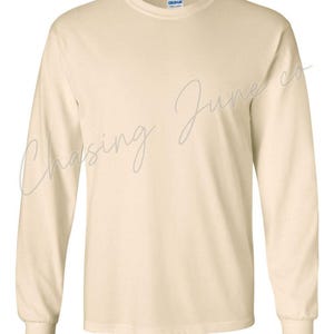 May include: A long-sleeved, cream-coloured shirt with a crew neck and ribbed cuffs. The shirt has the text "Chasing June co" in a cursive font across the front. The Gildan brand label is visible on the inside of the collar.
