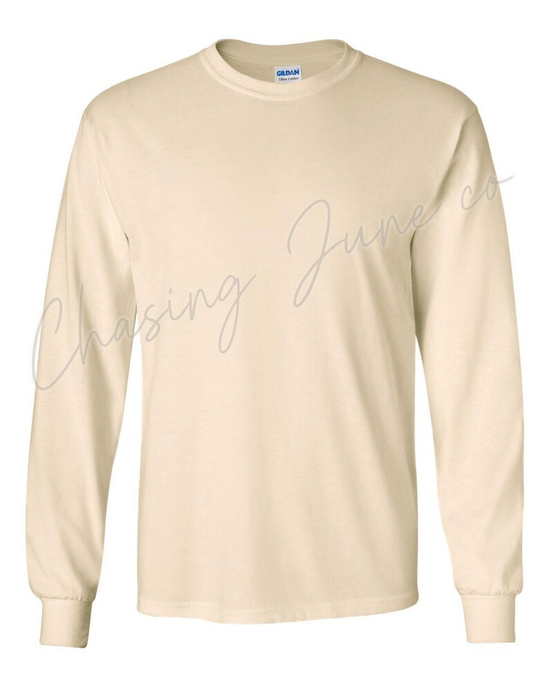 May include: A long-sleeved, cream-coloured shirt with a crew neck and ribbed cuffs. The shirt has the text "Chasing June co" in a cursive font across the front. The Gildan brand label is visible on the inside of the collar.