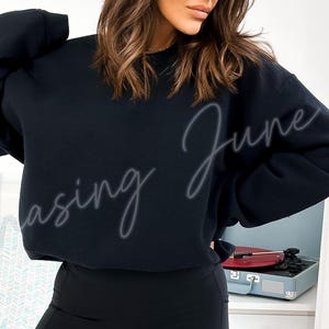 May include: A black sweatshirt with the text "Chasing June" in a cursive font. The sweatshirt is worn by a person. A record player is visible in the background.