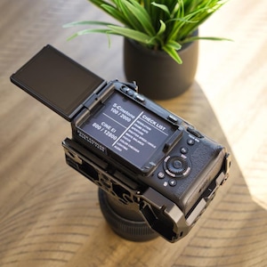 Puede incluir: Una cámara Sony FX3 negra con una pantalla abatible que muestra un menú con opciones para S-Cinetone, Cine EI, Resolución, Velocidad de fotogramas, Apertura, Velocidad de obturación/Ángulo, Balance de blancos, Enfoque, Comprobación de color, Iluminación y Audio.