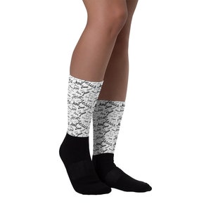 May include: White socks with a black and white print of the word "Jesus" repeated throughout. The socks are shown on a model's legs.