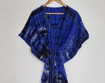May include: A blue and black tie-dye kaftan dress featuring a V-neckline, short wide sleeves, and a drawstring waist detail. The garment displays a vertical striped pattern created by the tie-dye process, with a fluid and loose silhouette.