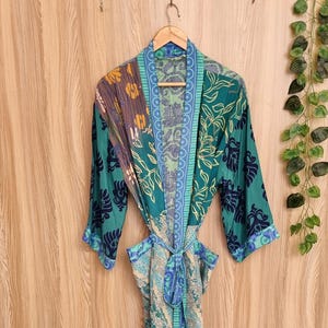 May include: A patterned robe with a tie waist hangs on a wooden hanger. The robe features a mix of teal, blue, and purple floral and geometric designs. The sleeves are three-quarter length.