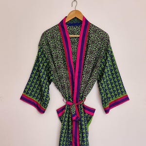 Peut inclure: Une robe à manches longues avec un motif géométrique répétitif dans des tons de vert, bleu et noir. Le vêtement présente une bordure rose vif le long de l'ouverture avant, des poignets et une ceinture à nouer assortie à la taille.