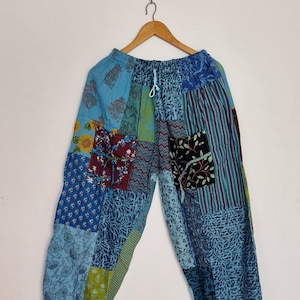 May include: Patchwork trousers featuring a variety of blue, green, and maroon fabric panels with diverse floral, striped, and geometric patterns. These pants have an elastic waistband with a light blue drawstring and gathered ankle cuffs.