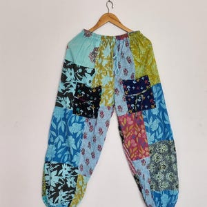 May include: Patchwork trousers featuring a variety of floral and botanical patterns in shades of blue, green, yellow, and pink. The trousers have an elasticated waistband with a drawstring, two front pockets, and elasticated cuffs at the ankles.
