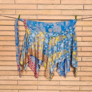 Könnte beinhalten: Ein farbenfroher Wickelrock mit geometrischem Muster in Blau-, Gelb- und Grautönen. Der Rock hat ein fließendes Design mit einem gemusterten Bindeband und hängt vor einer Backsteinmauer.