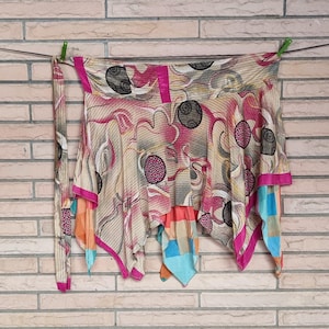 Puede incluir: Una falda envolvente colorida con un diseño único, con una mezcla de tonos rosas, beige y azules. La falda tiene una forma asimétrica y fluida con una cinta a juego. La tela está estampada con formas abstractas y ribeteada con bordes rosas brillantes.