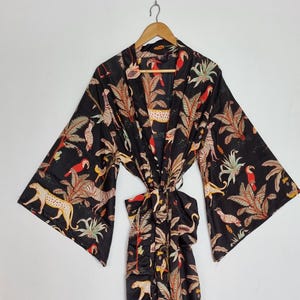 May include: A black kimono robe featuring a vibrant jungle print with spotted leopards, red parrots, and palm leaves. The garment has wide, three-quarter length sleeves, an open front design, and a matching fabric tie belt at the waist.