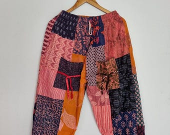 May include: Patchwork pants featuring a variety of fabric squares in shades of orange, pink, navy blue, and black. The garment has an elastic waistband with a drawstring, elasticized cuffs at the ankles, and two front pockets with small ties.