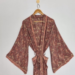May include: A long-sleeved robe featuring a muted red and brown paisley pattern throughout. The garment includes a matching fabric tie belt at the waist, wide sleeves, and a decorative border trim along the front opening and sleeve cuffs.
