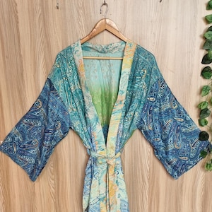 May include: A lightweight kimono robe featuring a vibrant gradient of teal, green, and blue hues. The garment is adorned with an intricate paisley pattern throughout, wide three-quarter length sleeves, and a matching fabric tie belt at the waist.