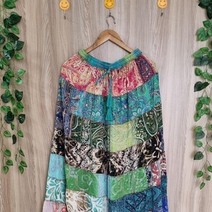 May include: A long, patchwork skirt with a variety of colorful paisley and floral patterns. The skirt is made of multiple fabric panels in shades of blue, green, pink, and purple. It hangs from a wooden hanger.