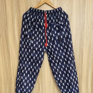 May include: Navy blue patterned trousers with a white floral design. The trousers have a red drawstring and are hanging on a wooden hanger. The fabric appears to be lightweight.