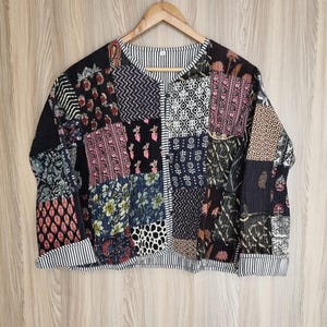 Puede incluir: Una chaqueta acolchada negra con un diseño de patchwork que presenta varios patrones florales y geométricos. La chaqueta tiene un cierre de botón y un ribete a rayas en los puños y el dobladillo.